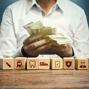 Person holding cash with various healthcare-related icons on wooden blocks in the foreground symbolizing Medical Malpractice Settlements in Louisiana - Porter & Guidry Law Firm