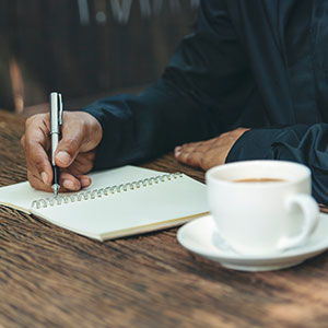 Person writing in a notebook with a cup of coffee on the table. - Porter & Guidry Law Firm