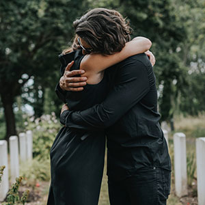Man and woman embracing in a graveyard, mourning the loss of their loved one.
